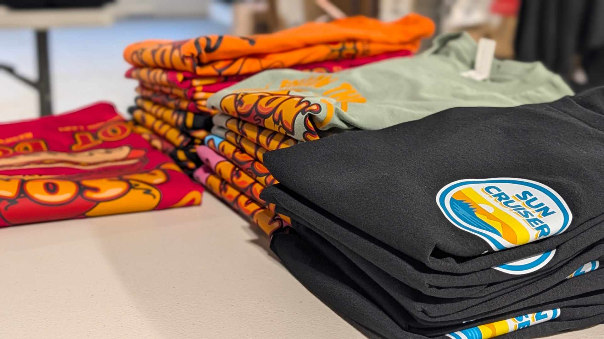 Stacks of freshly printed, folded tees in bold colors on a Hickory Brand House worktable